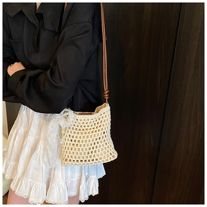 Détail du sac en paille beige avec pendentif perle blanche et noeud en dentelle délicat
