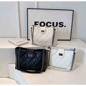 Trois sacs cabas matelassés en noir, blanc et beige sur un support d'exposition blanc
