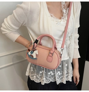 Dettaglio della borsa rosa con texture litchi e un ciondolo decorativo a forma di cavallo