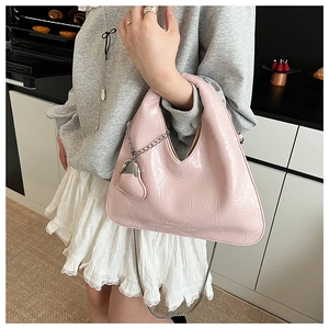 Close-up of pink glossy patent leather hobo bag with heart charm and metal chain strap