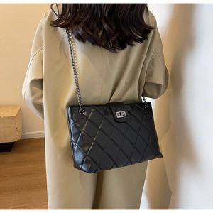 Dettaglio di una borsa tote nera trapuntata con tracolla a catena e trench beige