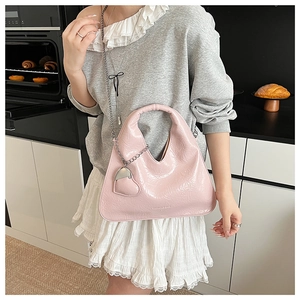 Detailed view of pink patent leather handbag with heart charm and thin metal chain strap