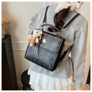 Détail d'un sac à dos en cuir noir gaufré avec un charme d'ours sur un mannequin