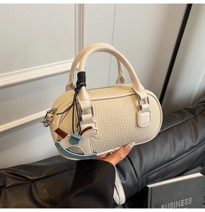 Dettaglio della borsa beige con grana litchi, ciondolo a cavallo e anelli metallici