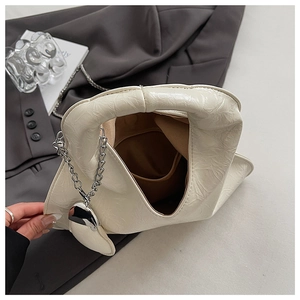 Detail of creamy white pleated leather handbag with silver chain and heart charm accessory
