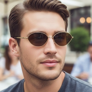 Retro golden metal oval sunglasses with dark lenses worn by a model in outdoor setting