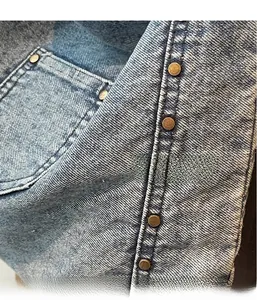 Detail of light blue washed denim fabric with copper rivets and durable stitching
