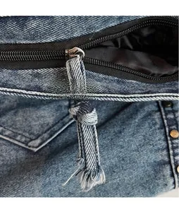 Close-up of denim shoulder bag featuring long tassel zipper pull with frayed edges