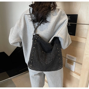 Detail shot of black washed denim tote with metallic studs and chain strap on shoulder