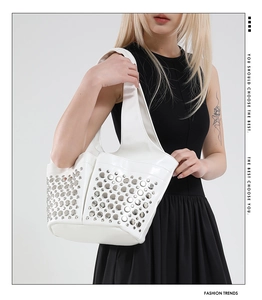 Close-up of a white leather bucket bag featuring silver rivet studs and a wide strap
