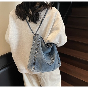 Detail of denim crossbody bag with vintage rivets and braided chain strap on a model