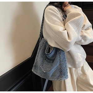 Macro view of washed blue denim tote bag featuring metallic stud details and chain strap