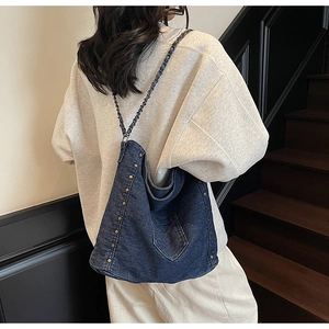 Detail of vintage blue denim tote bag with gold studs and chain strap on a model