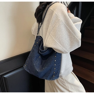 Detail of denim tote bag showing gold studs and black chain strap in a lifestyle shot