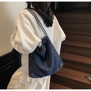 Detail of dark blue denim tote bag with metal studs and chain strap on female model