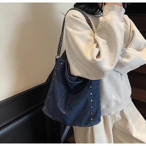 Detail of dark blue denim hobo bag with vintage gold rivets and chain woven strap