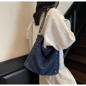 Detail of dark blue denim tote bag with metal chain strap and vintage bronze rivets