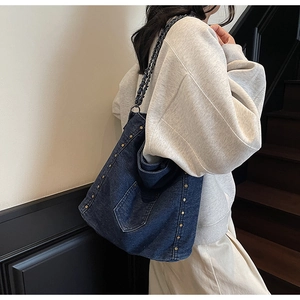 Detail of dark blue denim tote bag with metal studs and chain strap on a model