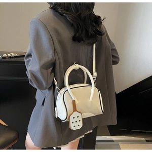 Detalle de un bolso Boston blanco crema con asas dobles y un colgante de cuero decorativo