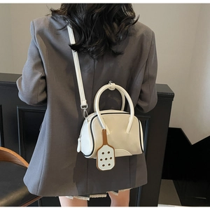 Rear view of a model carrying a white bowling-style crossbody bag with a decorative charm