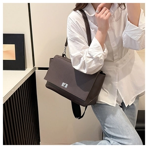 Detail of dark brown leather crossbody bag with silver square lock on white shirt