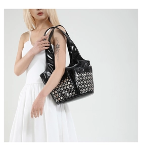 Detail of black patent leather tote bag with silver studs on model with white dress