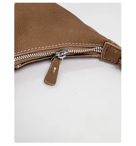 Detail of smooth metal zipper and white stitching on brown litchi pattern leather bag