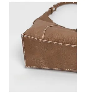 Detail view of reinforced brown lychee leather bottom with white stitching on shoulder bag