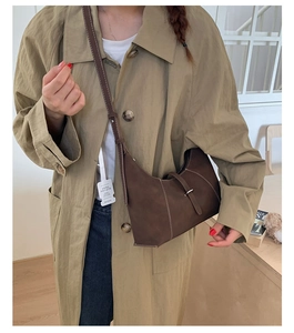 Detail of a brown matte crescent shoulder bag with metallic buckle on tan trench coat
