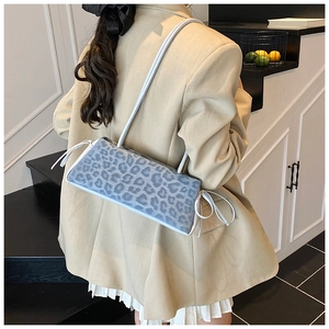 Blue leopard print baguette bag with side string details worn by a model in a beige suit