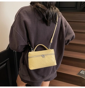 Detail of light yellow quilted crossbody bag with top handle and gold hardware