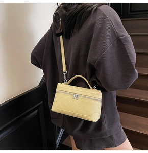 Detail of light yellow quilted vanity bag featuring silver zippers and leather top handle