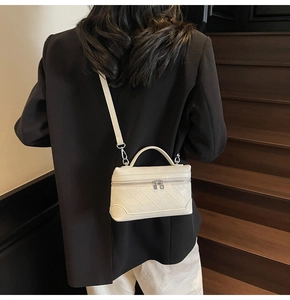 Rear view of cream quilted crossbody bag with top handle worn by model on stairs