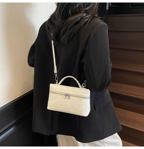 Detail of a chic cream-colored box bag with mesh texture worn over a black blazer