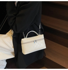 Close-up of cream square handbag with quilted pattern and metal strap hooks