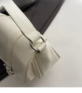 Detail of silver metal hardware and fine stitching on a creamy white leather crossbody bag