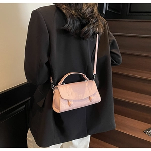 Pink lychee grain leather crossbody bag with round handle shown on a black blazer