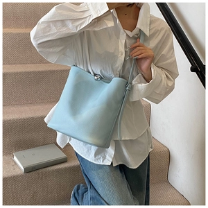 Mannequin portant un sac seau bleu clair avec fermoir boule argenté dans un escalier