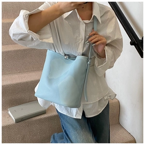 Détail d'un sac seau bleu clair en cuir avec fermoir boule en métal et texture grainée