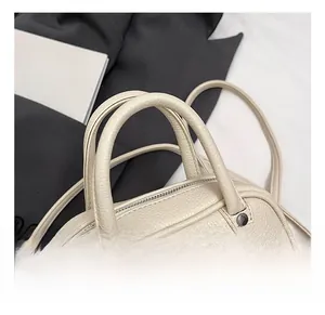 Detail of lychee textured leather pillow bag with round handles and silver zippers