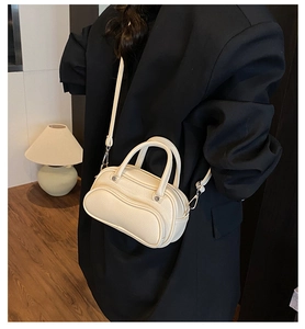 Detailed side view of off-white lychee grain crossbody bag worn with a black suit