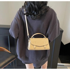 Detail view of a beige crossbody bag with lychee texture worn by a model in gray outfit