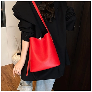 Détail d'un sac seau en cuir litchi rouge avec fermoir boule argenté sur un blazer noir