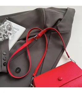 Detail of red lychee textured crossbody bag with adjustable strap on grey suit blazer