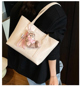 Detailansicht einer beigen Kunstleder-Totetasche mit Textur und einem süßen Plüschanhänger.