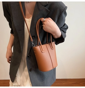 Brown litchi texture bucket bag worn by model with adjustable crossbody strap