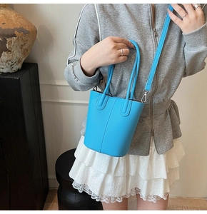 Detail of bright blue lychee textured leather bucket bag styled on a wooden display