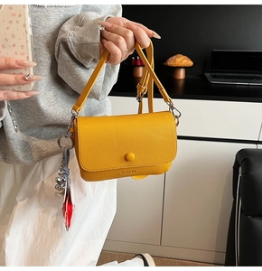 Close-up of bright yellow litchi pattern leather bag with decorative heart charm and strap