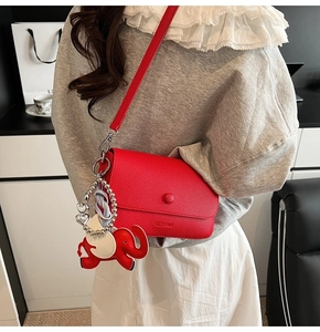 Close-up of red lychee leather bag with cute elephant charm on a shoulder strap