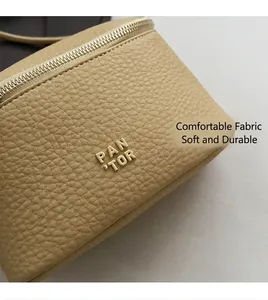 Dettaglio della pelle beige a grana litchi con logo metallico dorato e zip lucida